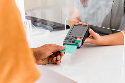 Cropped unrecognizable female specialist holding card reader while male patient paying for treatment with credit card in modern clinic