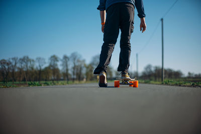 Low section of man skateboarding on road against sky