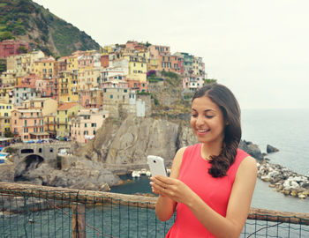 Portrait of smiling young woman using mobile phone against sea