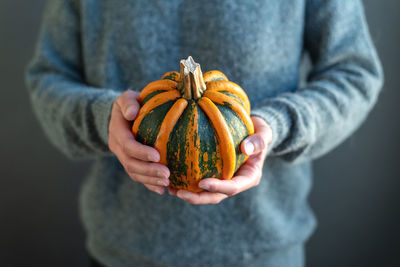 Women's hands hold a bright orange and green pumpkin.