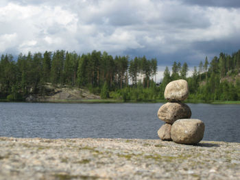 Stack of pebbles on rock by lake against sky