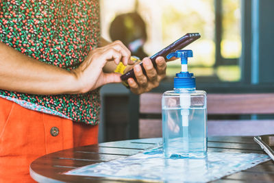 Midsection of woman holding glass while sitting on table