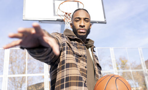 Low angle portrait of man standing against basketball hoop against sky