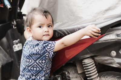 Portrait of cute boy standing by covered motorcycle