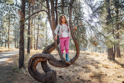 Girl in rubber boots and sweatpants climbing pine tree in forest