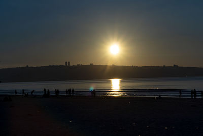 Silhouette people on beach against sky during sunset