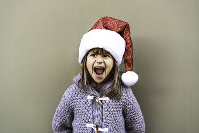 Girl wearing santa hat with mouth open standing against wall