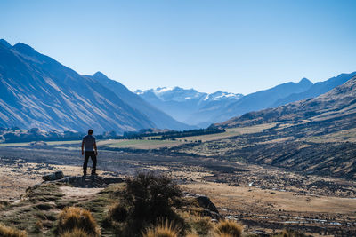 Rear view of man standing on rock against mountains and clear sky