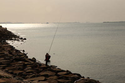 Fishing rod on rock by sea against sky