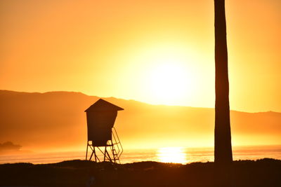 Silhouette built structure by sea against orange sky