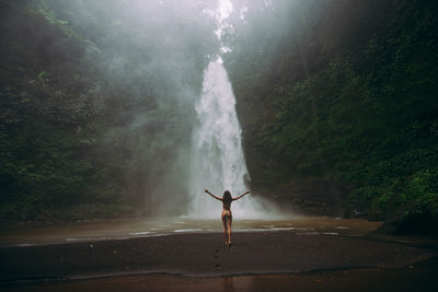 Young woman standing against waterfall