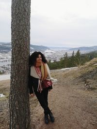 Woman leaning on tree against sky during winter