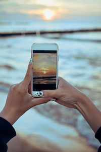 Young woman taking photos of sunset over sea using smartphone during summer trip