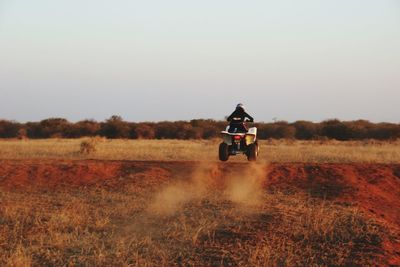 Rear view of man riding quadbike on field against clear sky