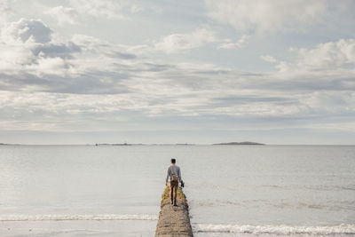 Rear view of man walking on pier in sea against sky