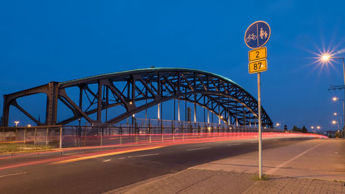 Light trails by bridge on road against sky at dusk