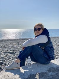 Portrait of smiling girl sitting by sea against sky