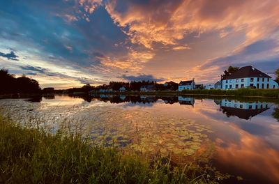 Scenic view of lake by buildings against sky during sunset