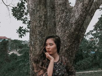 Portrait of beautiful young woman against tree trunk