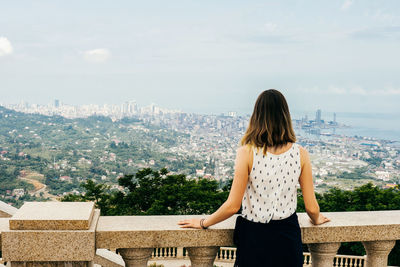 Rear view of woman looking at cityscape against sky