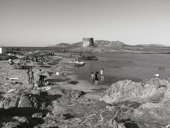 People on rocks by sea against clear sky