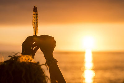 Close-up of woman holding feather at beach against sky during sunset