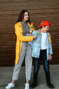 A girl in a yellow raincoat and a boy in a red cap are holding colorful ice cream in their hands