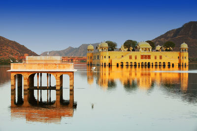 Jal mahal in lake by mountains against clear blue sky