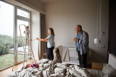 Woman and grandfather looking at baby boy standing on ladder in bedroom at home