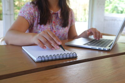 Midsection of woman using phone while sitting on table