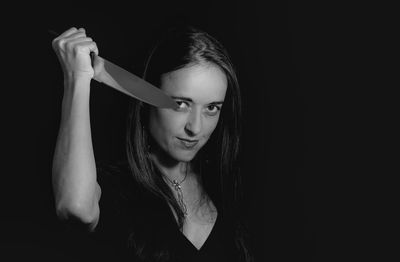 Portrait of young woman holding knife against black background