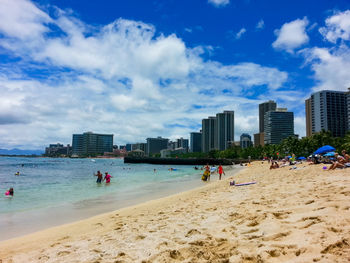 People on beach against sky in city