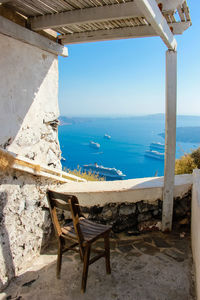 Chair on table by sea against clear sky