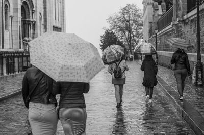 Rear view of people walking on wet road during rainy season