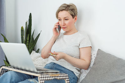 Young woman using laptop while sitting on sofa at home