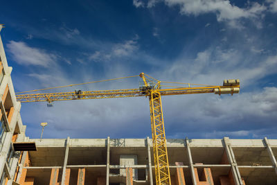 Low angle view of crane by building against sky