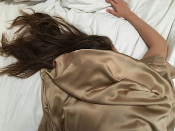 High angle view of girl covered with satin sheet while sleeping on bed