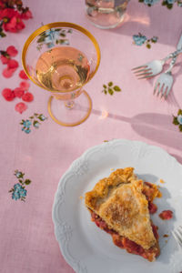 Single slice of rhubarb pie on white plate, pink tablecloth with blue roses, rose wine 