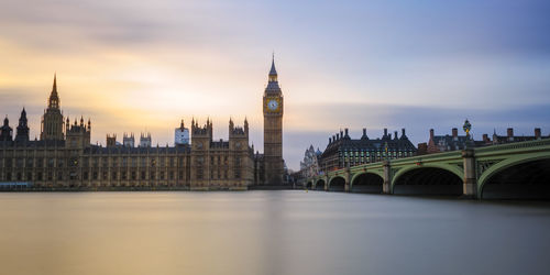 Westminster bridge over thames river by big ben and houses of parliament against sky during sunset