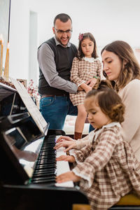 Adorable toddler child with mom playing piano against smiling father embracing daughter in house room