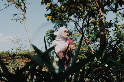 Young woman wearing hijab sitting by trees on field