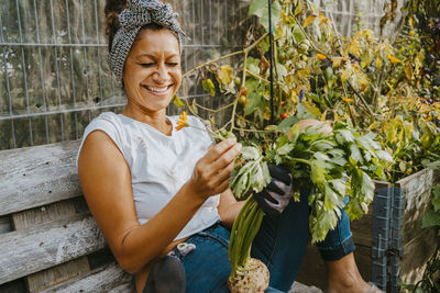 Happy female environmentalist with vegetable sitting in urban farm