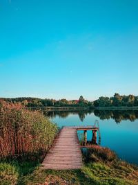 Pier over lake against clear blue sky