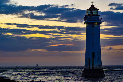 Lighthouse by sea against sky during sunset