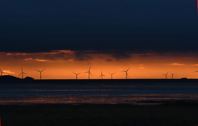 Silhouette wind turbines on field against sky at sunset