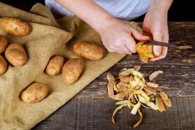 Midsection of man peeling potatoes on wooden table