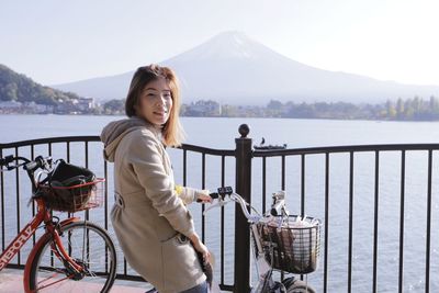 Portrait of smiling young woman with bicycle against river
