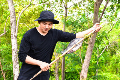 Man holding stick with fish while standing against trees in forest