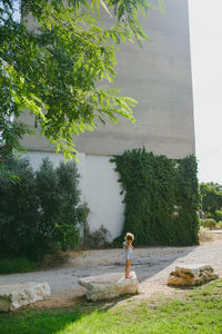 A young girl covering her face while standing on a stone outside