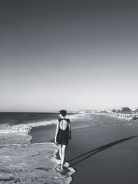 Rear view of woman walking on beach against clear sky